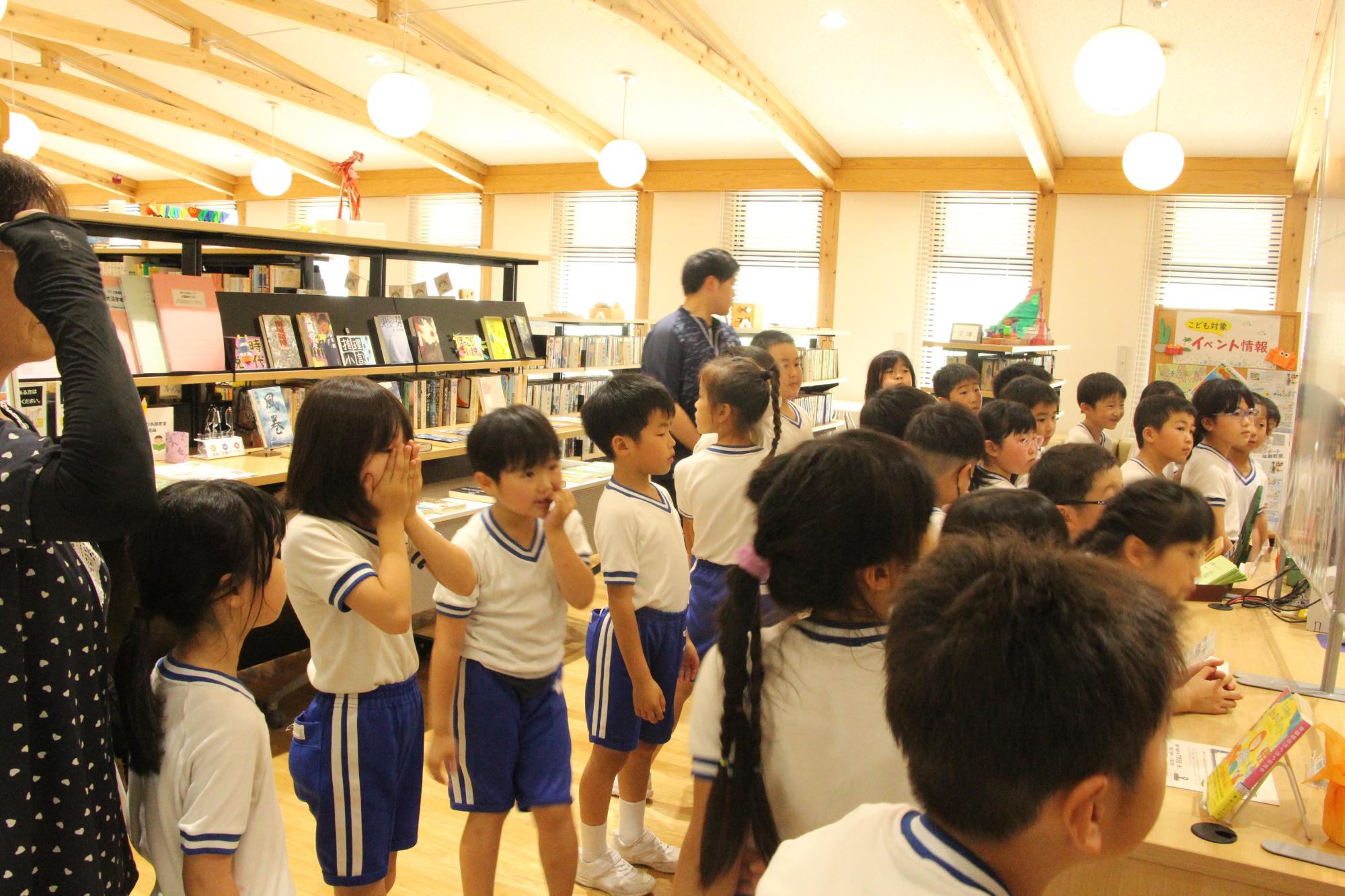いちのぴあ図書室に児童らが集まり、その特徴や利用方法を市の職員に尋ねている写真