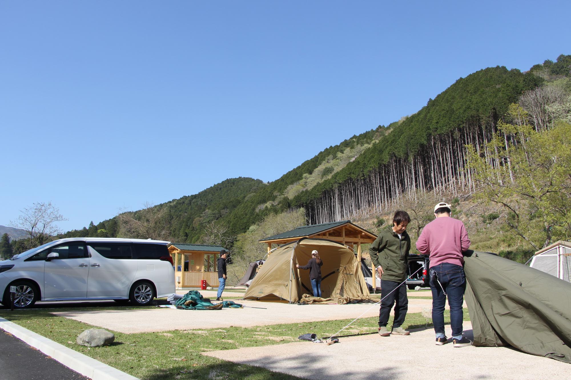 キャンプ場を利用する2人の男性がテントを広げて設営を始めている写真