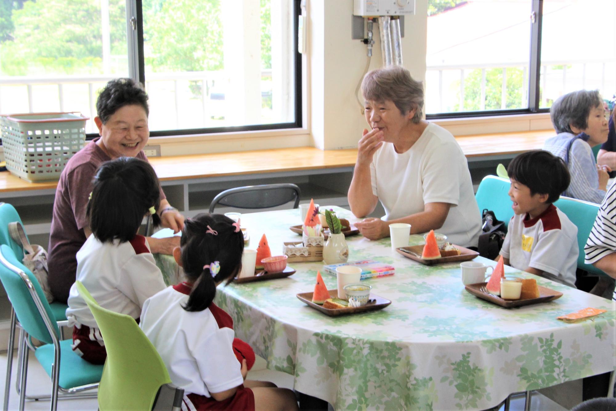 テーブルを囲んで座る園児と地域住民がプレートメニューを味わいながら会話を楽しんでいる写真