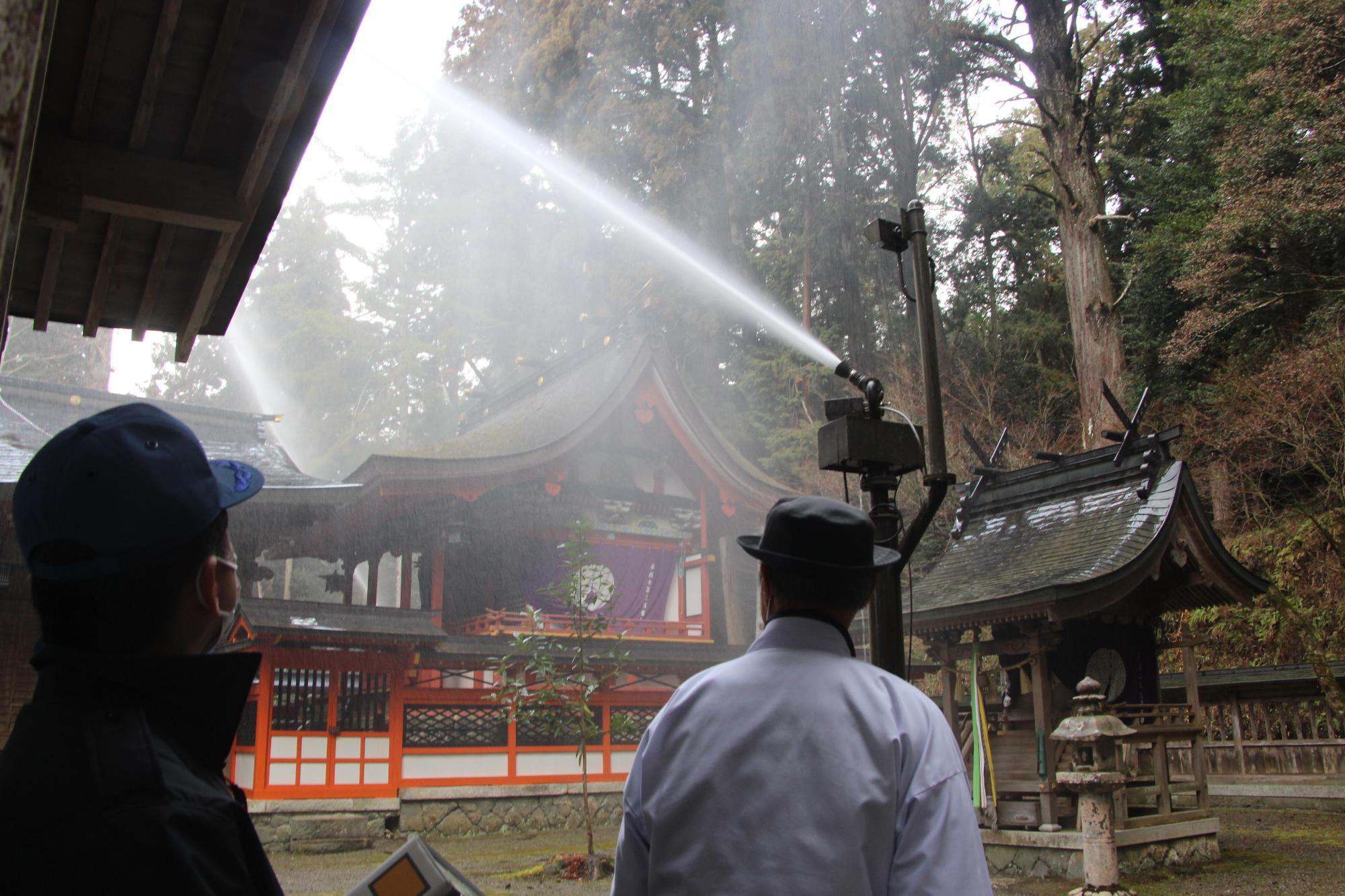 御形神社の放水銃を作動させ動作確認をする消防署職員と進藤宮司の写真