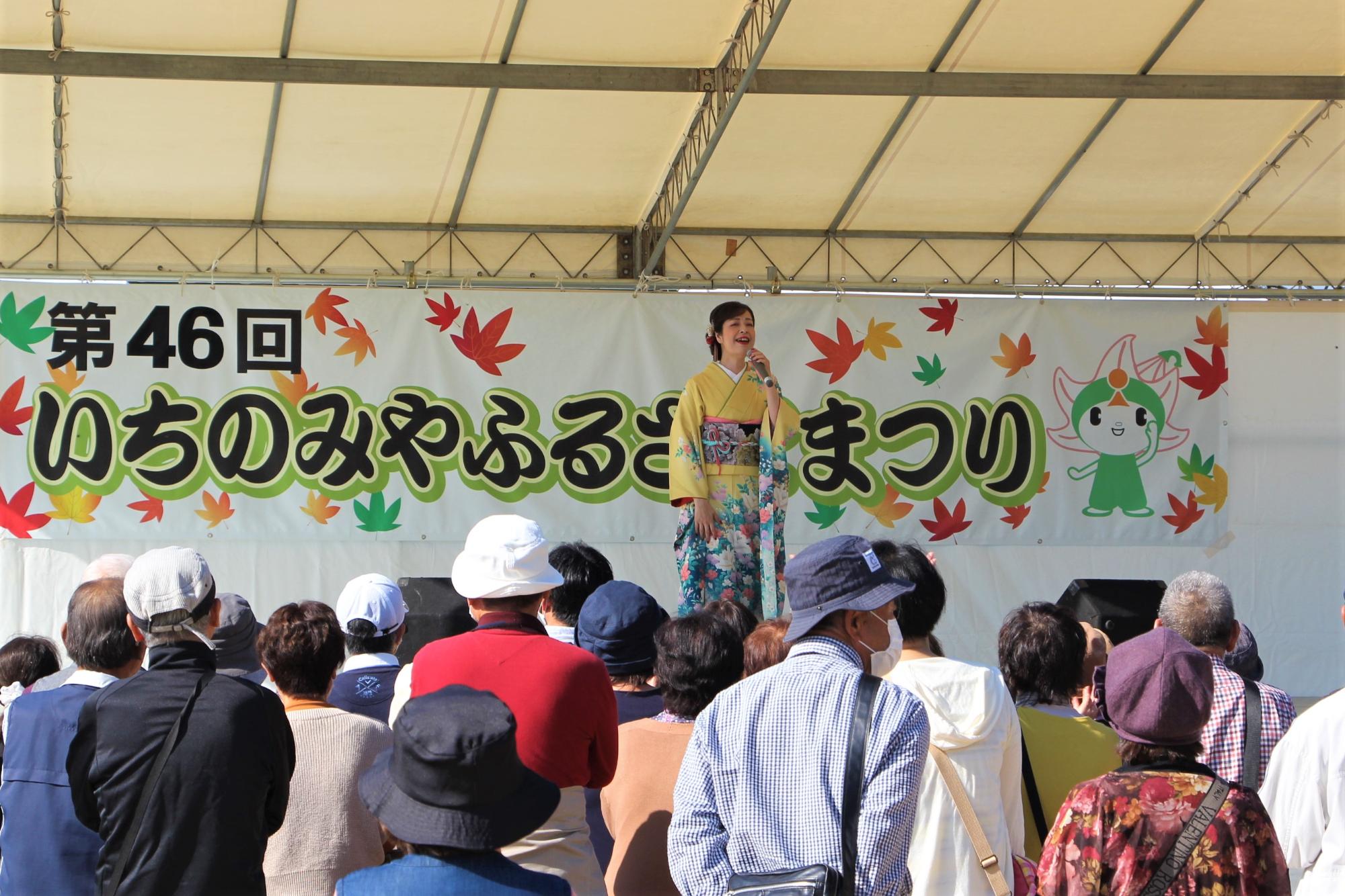観光大使の瀬口侑希さんの歌声にステージ前に集まった来場者が聞き入っている写真