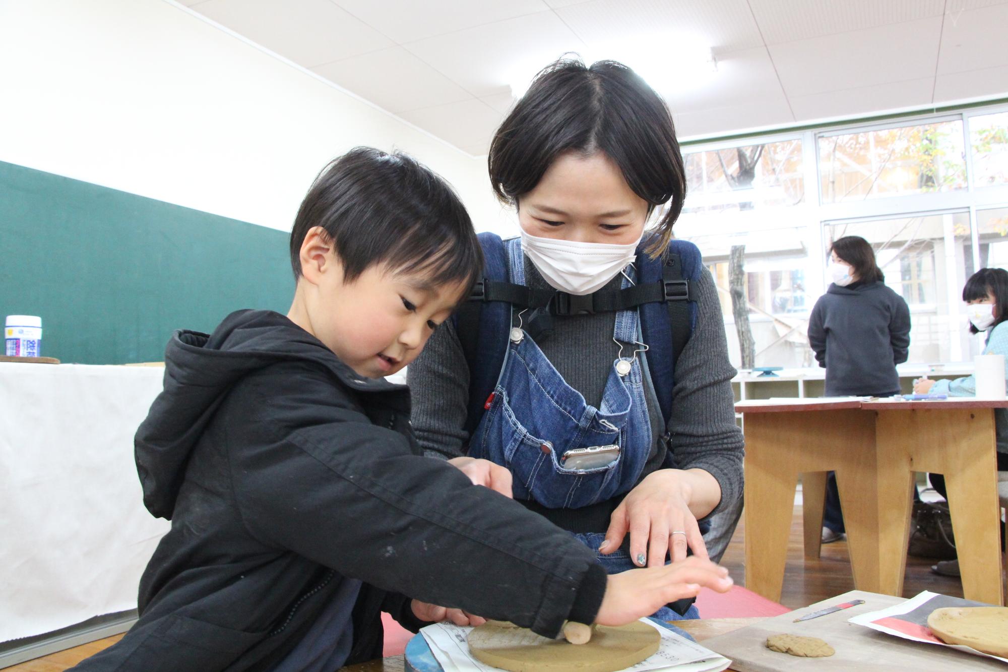 陶芸体験教室でお皿の形にこねた土を伸ばしている母親と男の子の写真