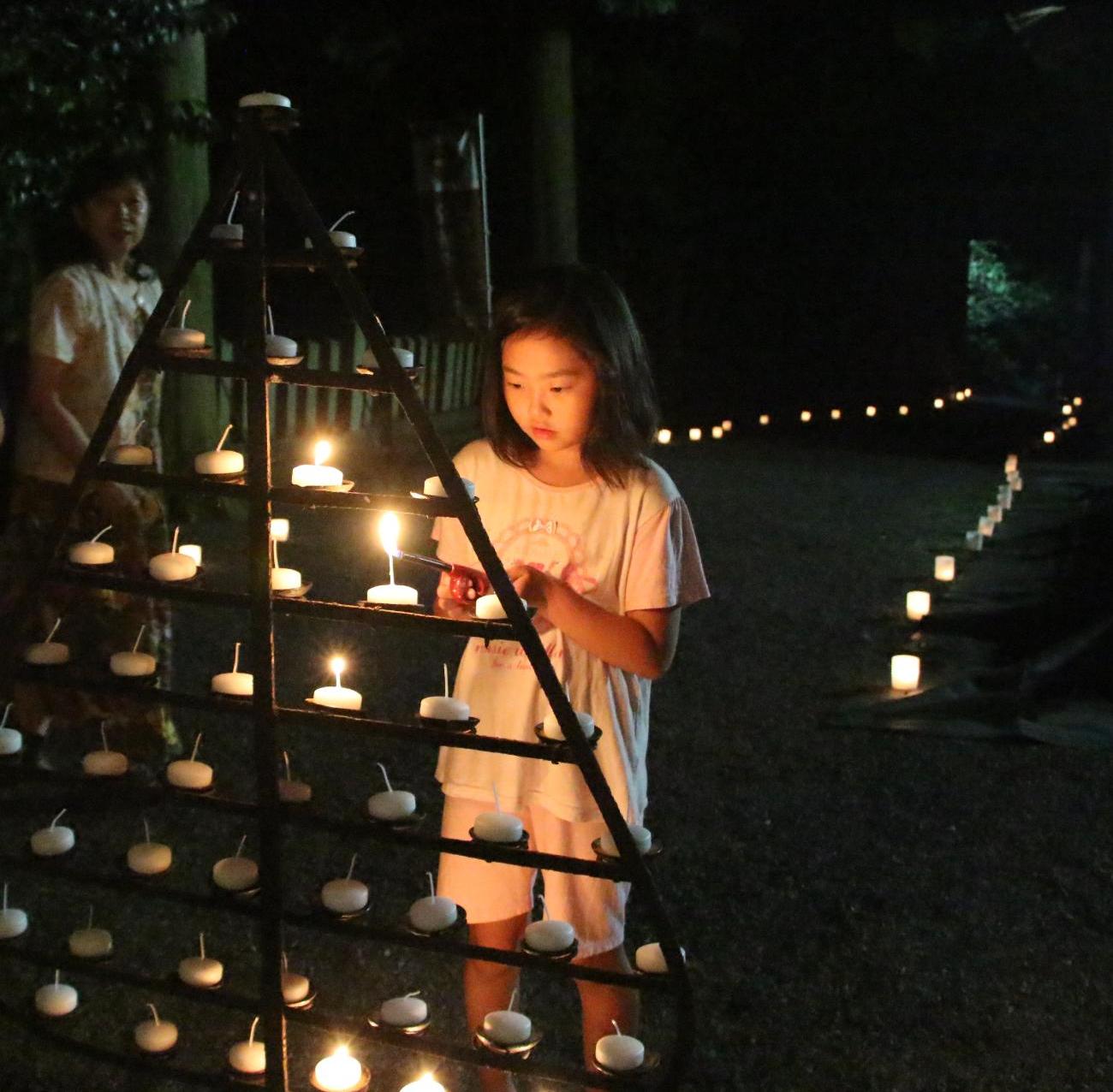 ツリー状に並べられた灯明に明かりをつける女の子の写真