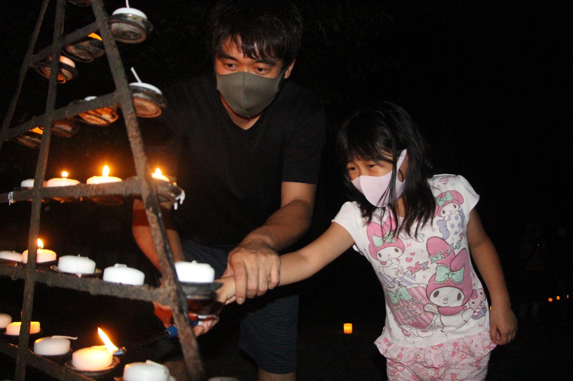 庭田神社の八朔祭りで髪の長い女の子と父親がろうそくに手を伸ばし一緒に火を灯している写真