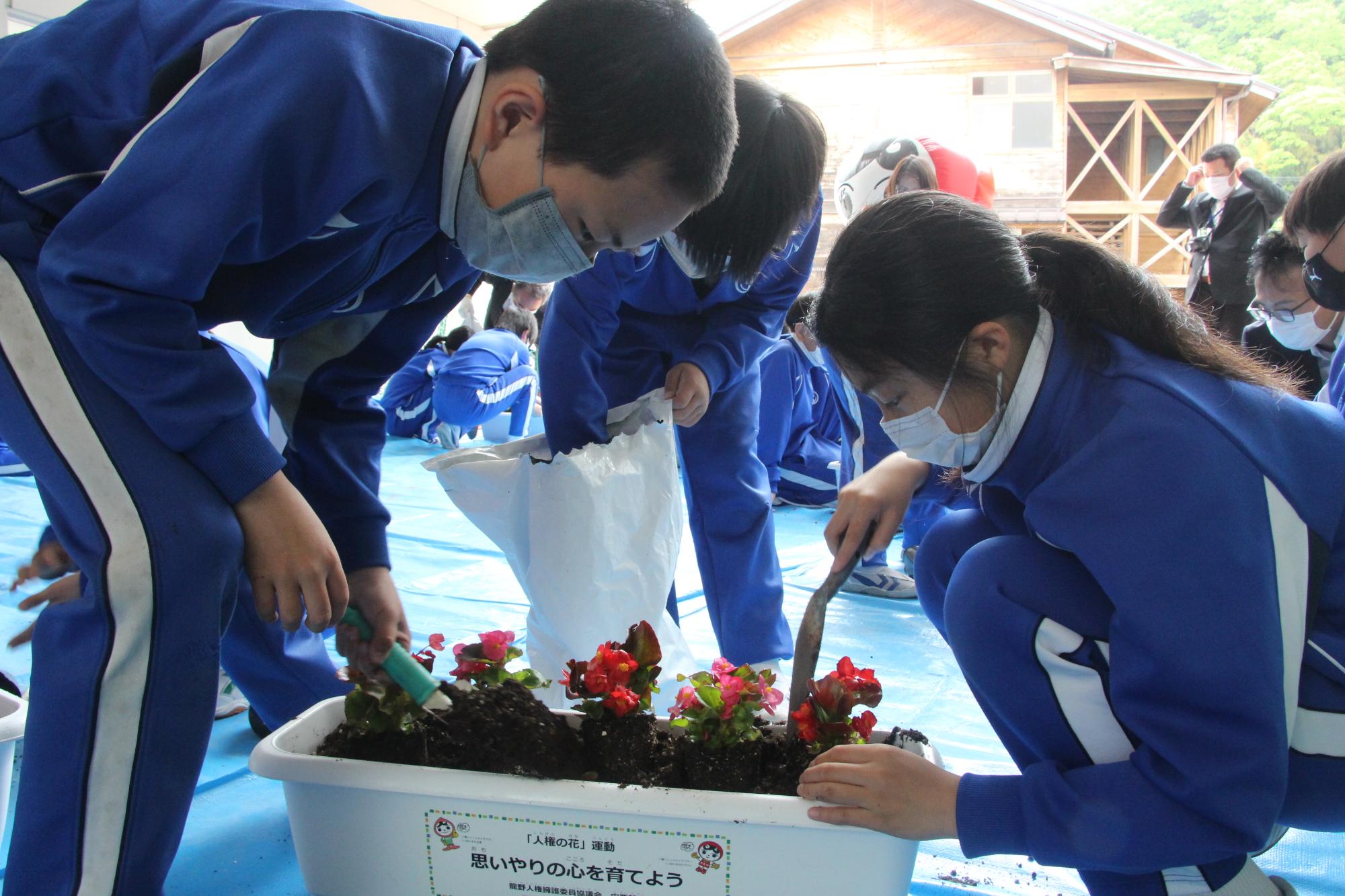 プランターに植えた花を苗に協力して土をかぶせている小学生の写真