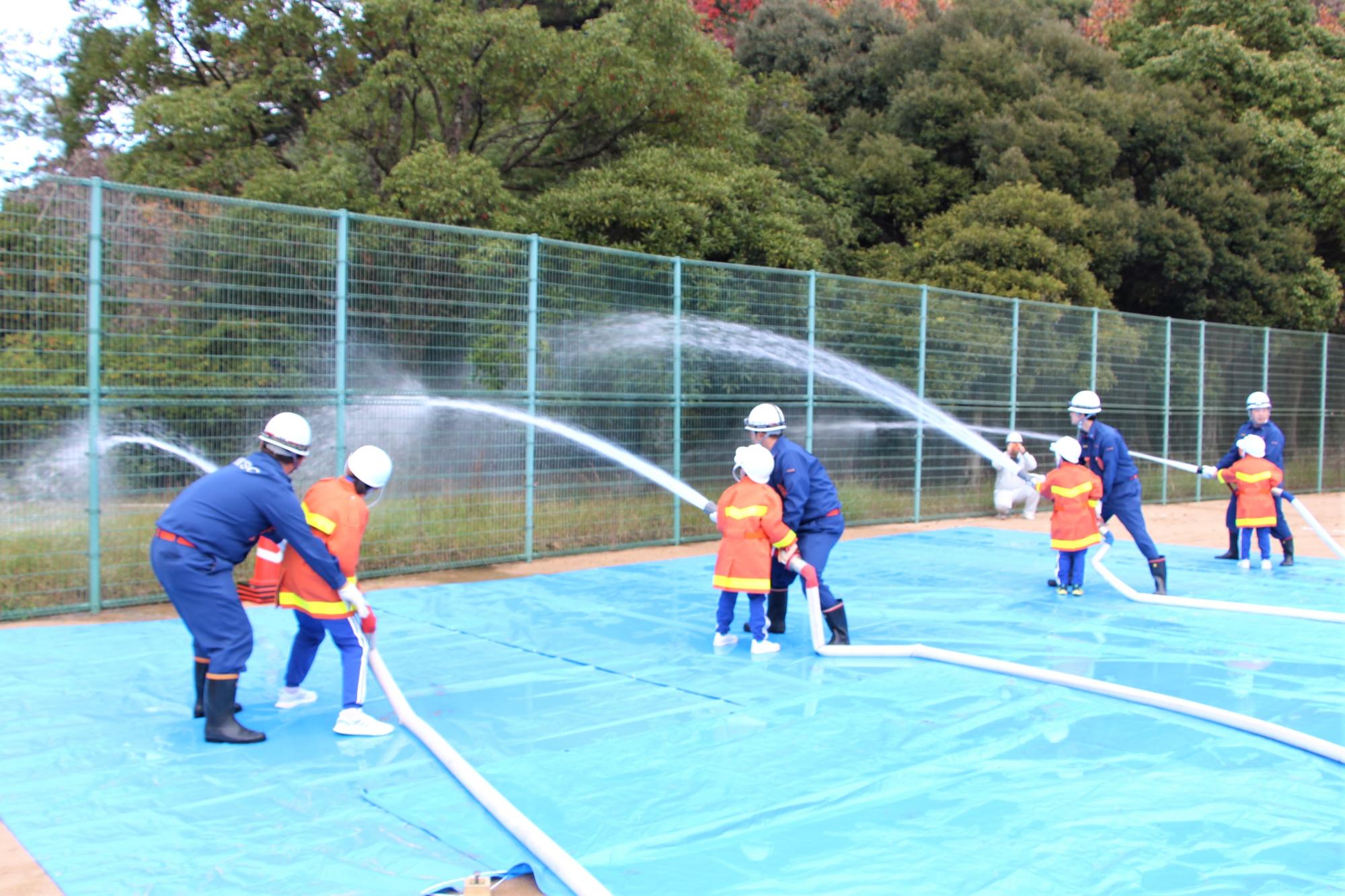 消防団員に手ほどきを受けながら放水体験をするはりま一宮小学校児童の写真