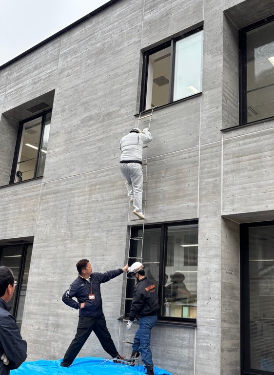 市職員が避難はしごを使って窓から降りる訓練している写真