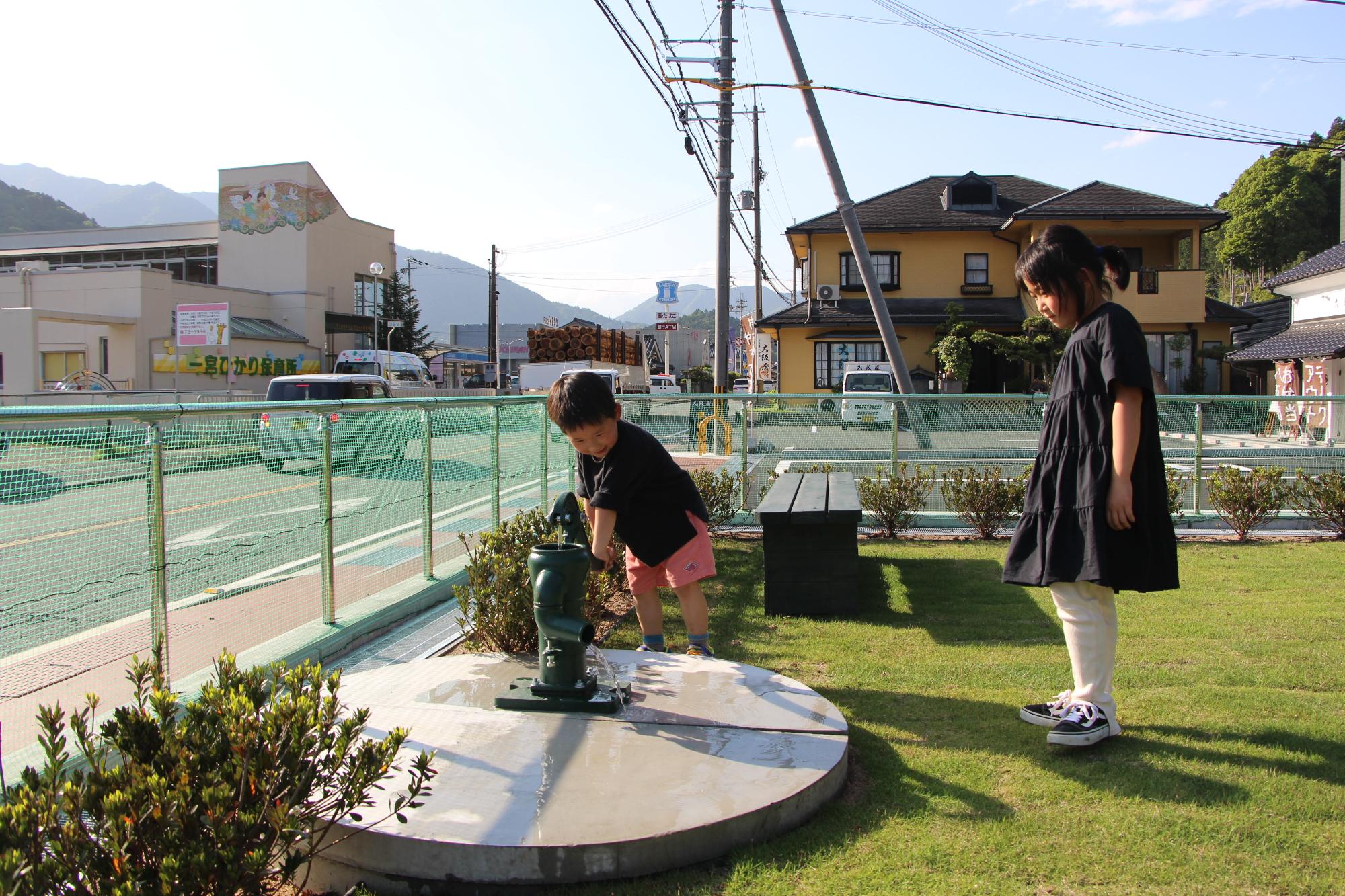 手押しポンプで水を出して遊んでいる子どもとそれを見守る保護者の写真