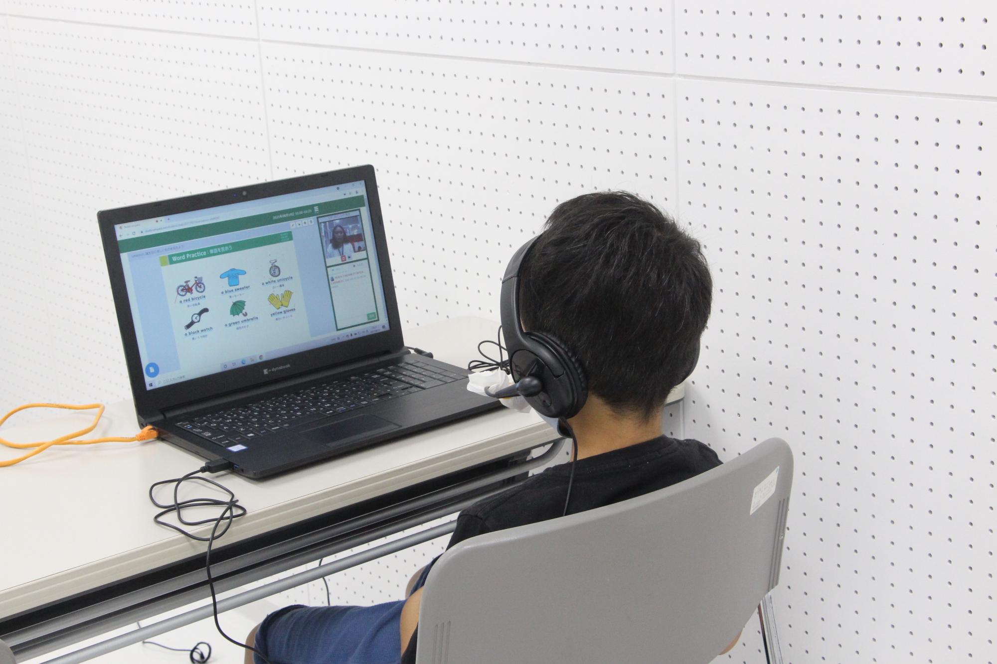 ヘッドホンをつけた子どもがパソコンの画面に向かいオンライン英会話教室に参加している写真