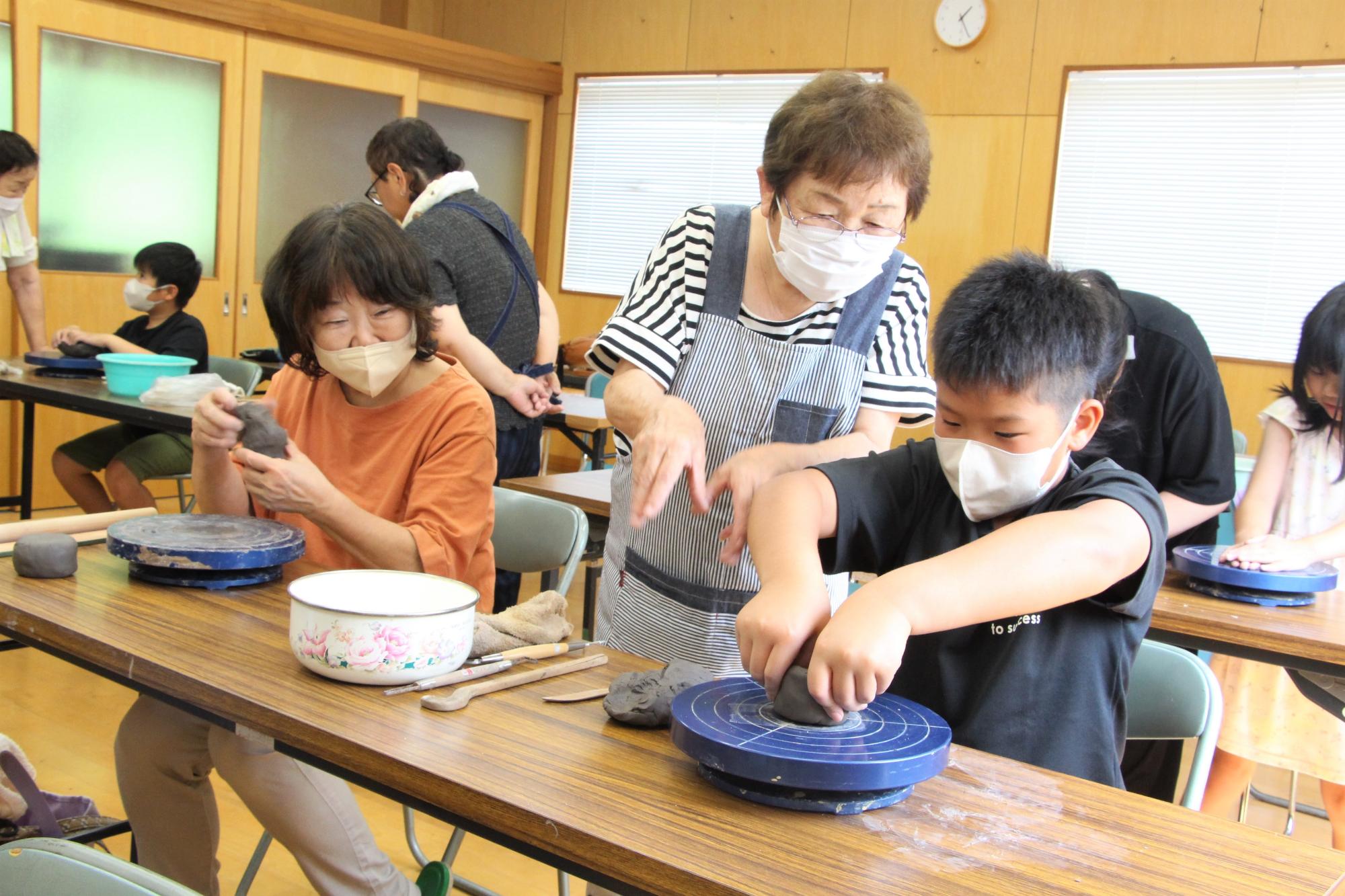真剣な表情でろくろの上の粘土を形成する小学生の写真