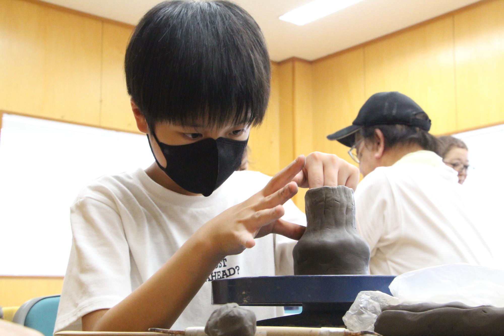 真剣な表情でろくろの上の粘土を形成し湯呑の形を作っている参加者の写真