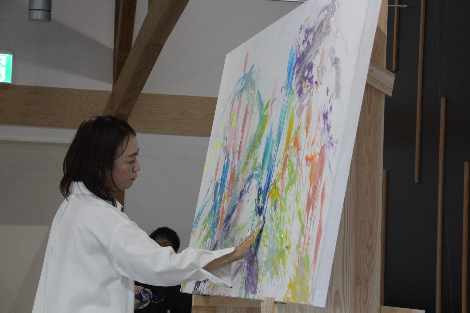 植田さんがキャンバスに、手の指をつかって色を塗っている写真