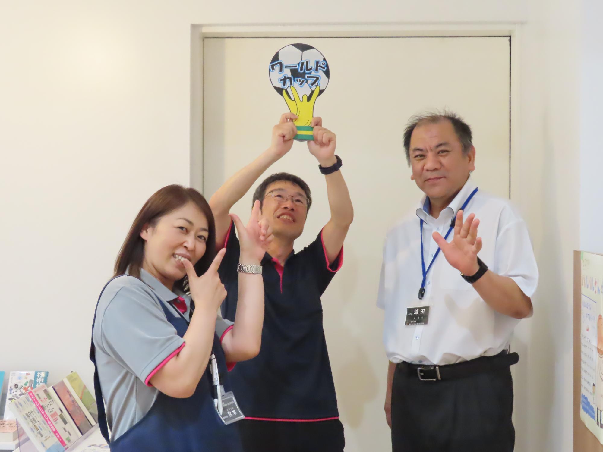優勝トロフィーを模した厚紙を掲げる職員