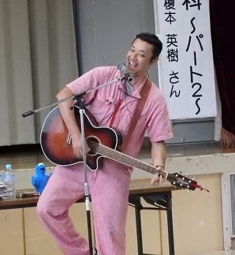 大学院6月講座でギターを持って歌を披露する講師の写真