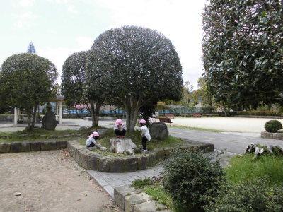 本多公園の植木で遊ぶ淡いピンク色の防止をかぶった3人の幼児の写真