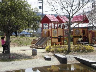 カラフルなプラスチックでできた滑り台などをふくむ複合的な遊具や広葉樹がある夢公園の写真