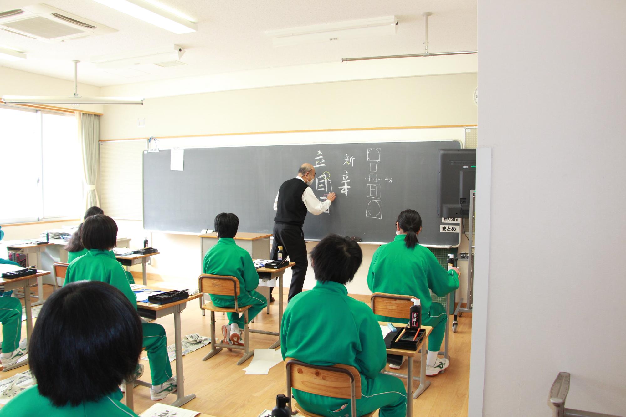 黒板にワンポイントアドバイスを書く先生とそれを見つめる生徒ら