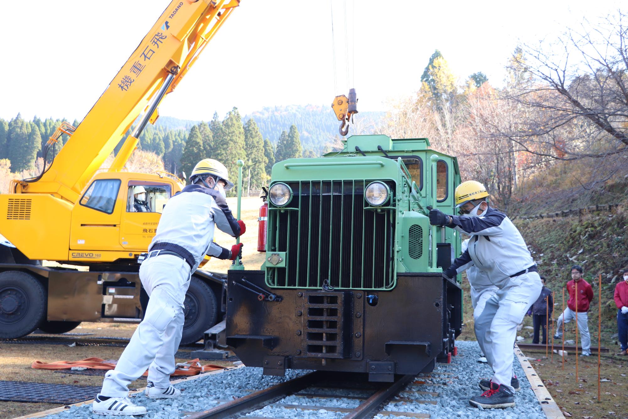 レールに設置された機関車を動かす作業員の写真