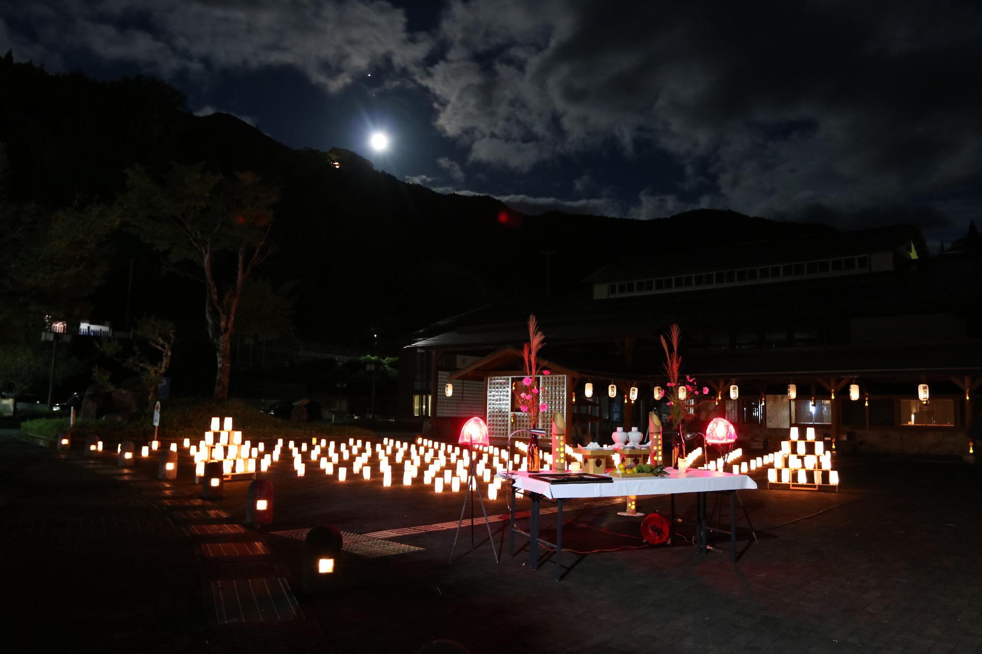 月の下で波賀市民局前に並んだ250個の灯篭の明かりが夕闇に浮かんでいる写真