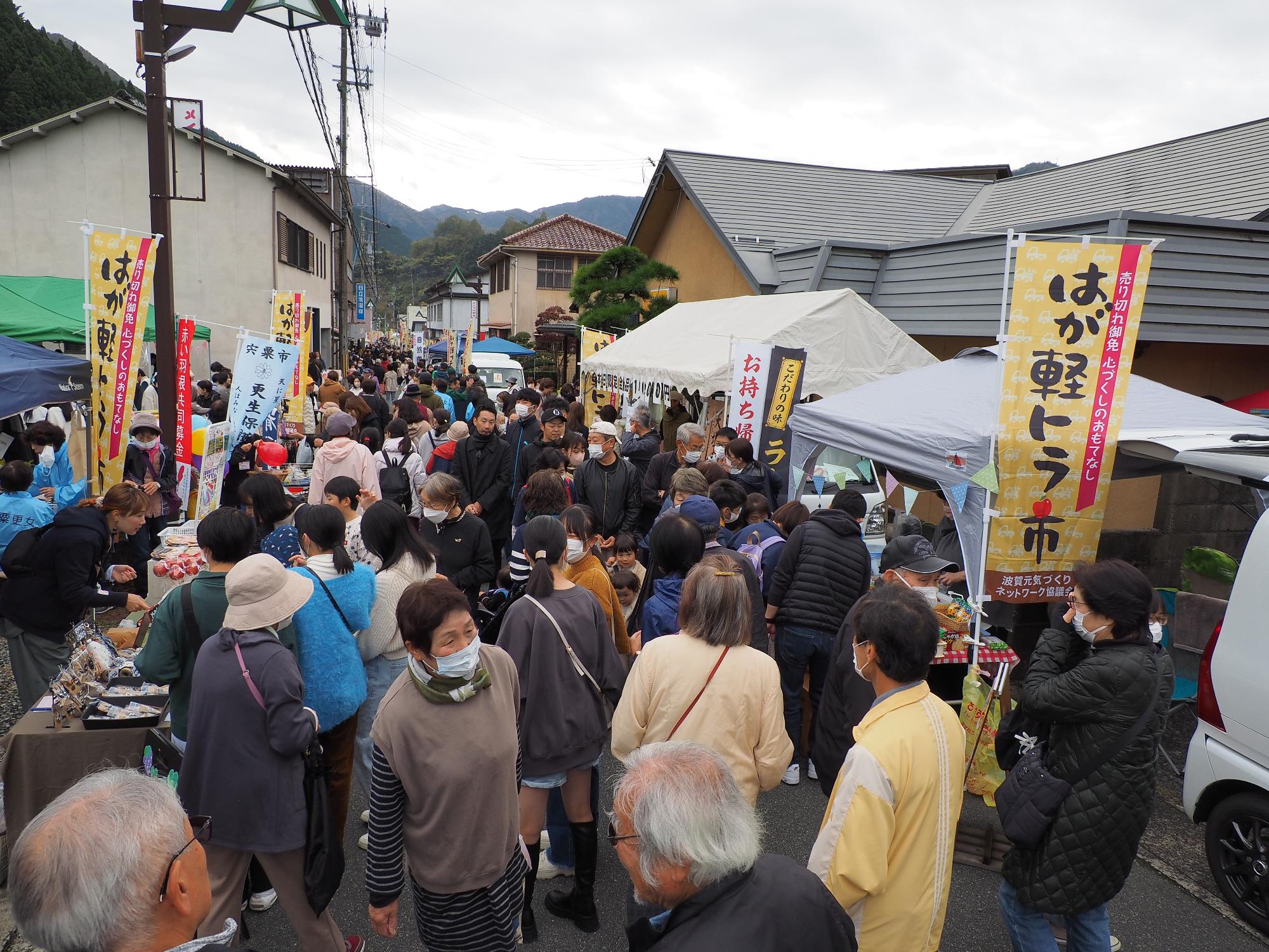 出店者の軽トラやテントが通りの両脇に並び、その間を通りいっぱいに広がって来場者が歩いている写真