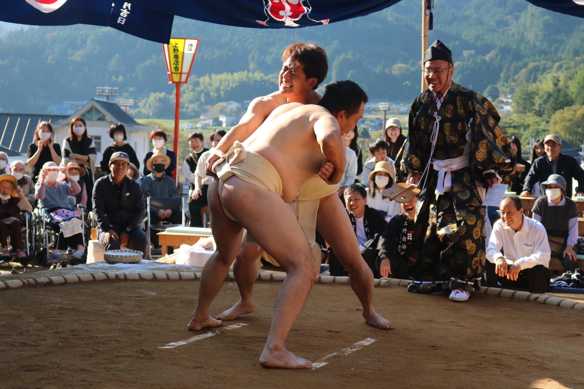 対戦している2人の力士が土俵上で組み合っている写真