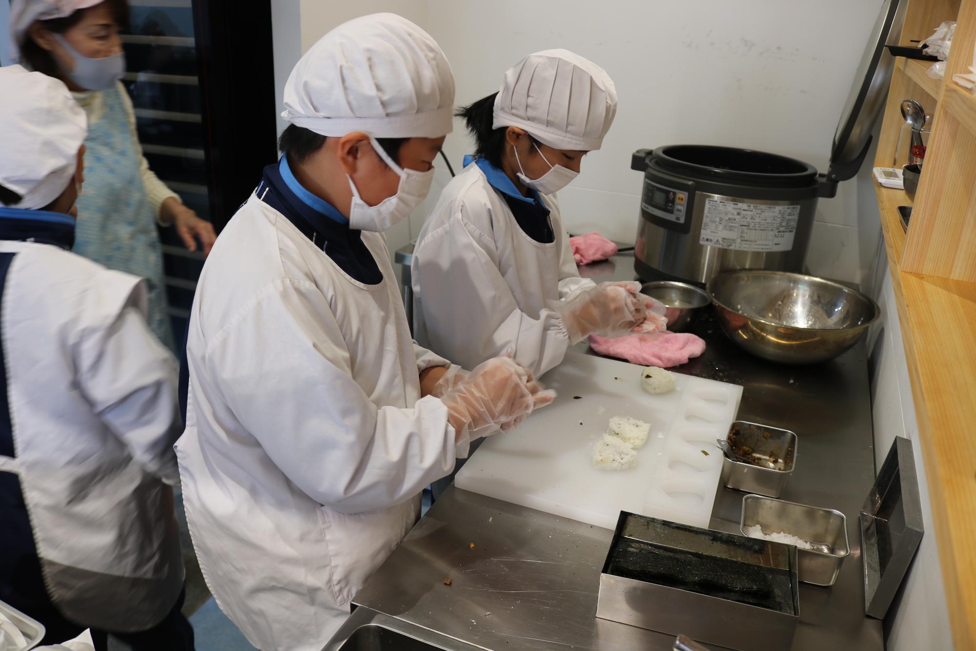 お店の厨房で2人の児童が炊いたご飯を「こにぎり」をにぎる児童