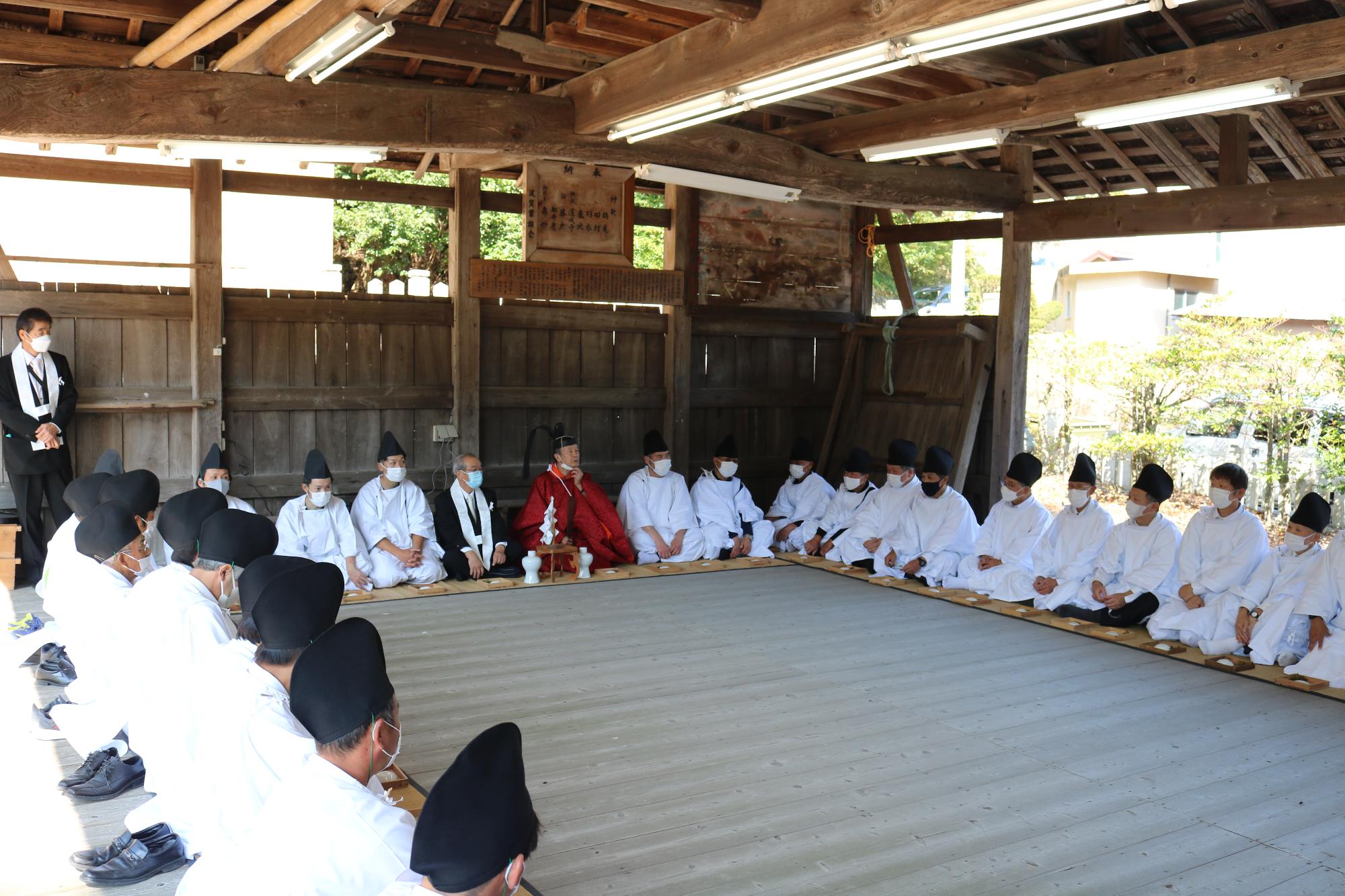 大座の式に神主、宮総代、75役の人が集まり、座って出陣式のようなものを行っている写真