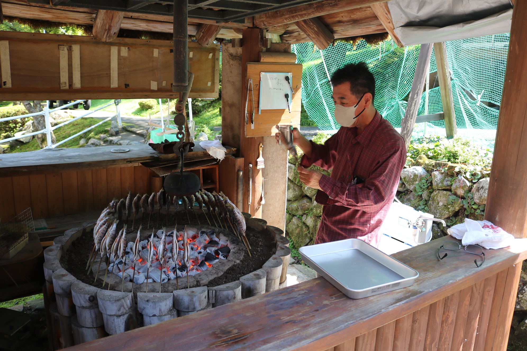 施設のスタッフが竹串を通したヒラベを炭火の周りに並べて塩焼きにしている写真