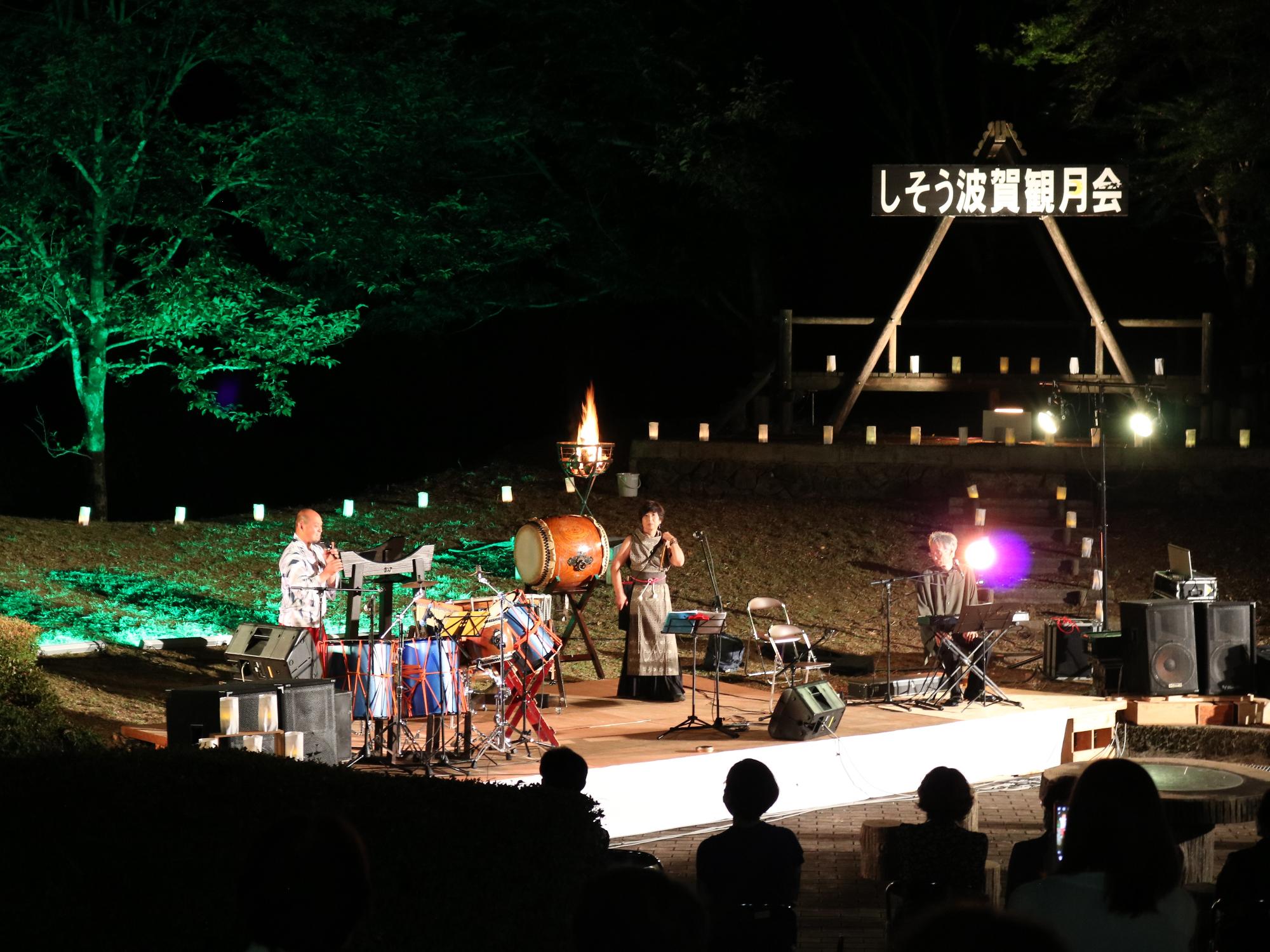 観月会ステージで和太鼓など楽器が並び、演者があいさつしている写真