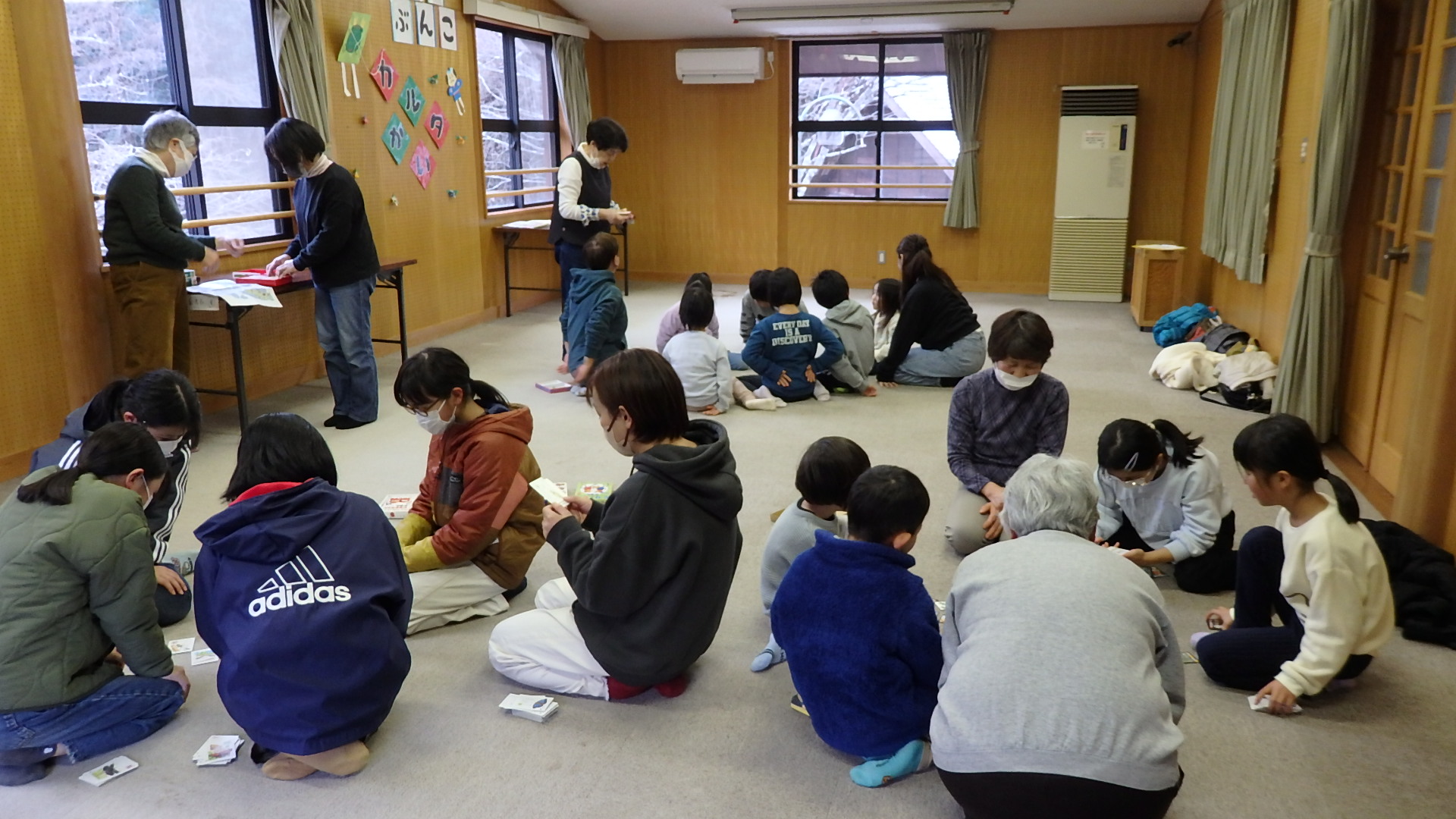 参加者らが座ってかるたの絵札を囲み、句が読み上げられるのを待っている写真