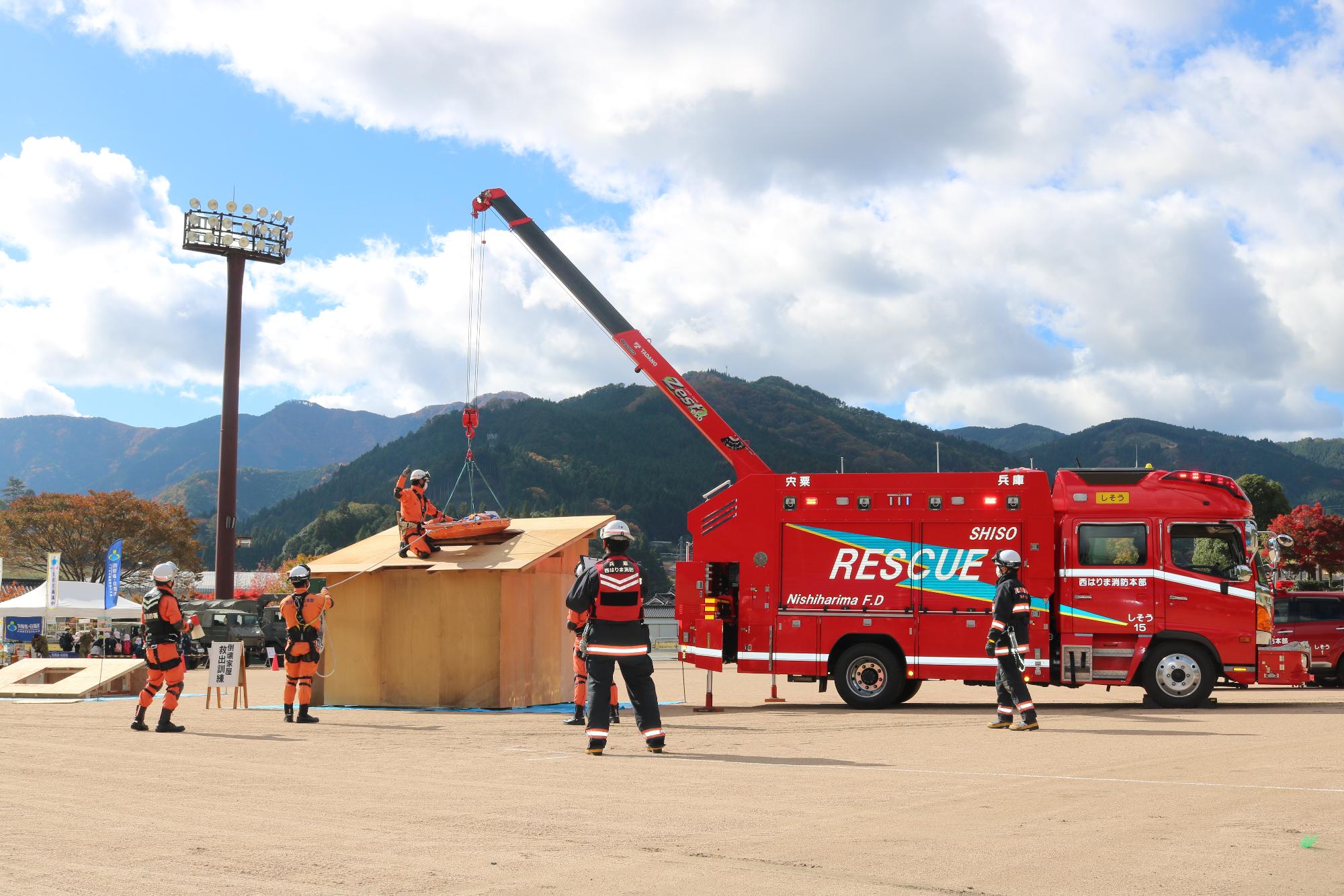 レスキュー車のクレーンをつかて消防隊員が倒壊家屋を想定した仮設建物の屋根から降りている写真