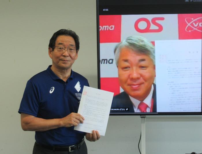福元市長とスクリーンに映し出される株式会社オーエスエムの奥村社長がそれぞれサインを交わした協定書を手に持って微笑んでいる写真