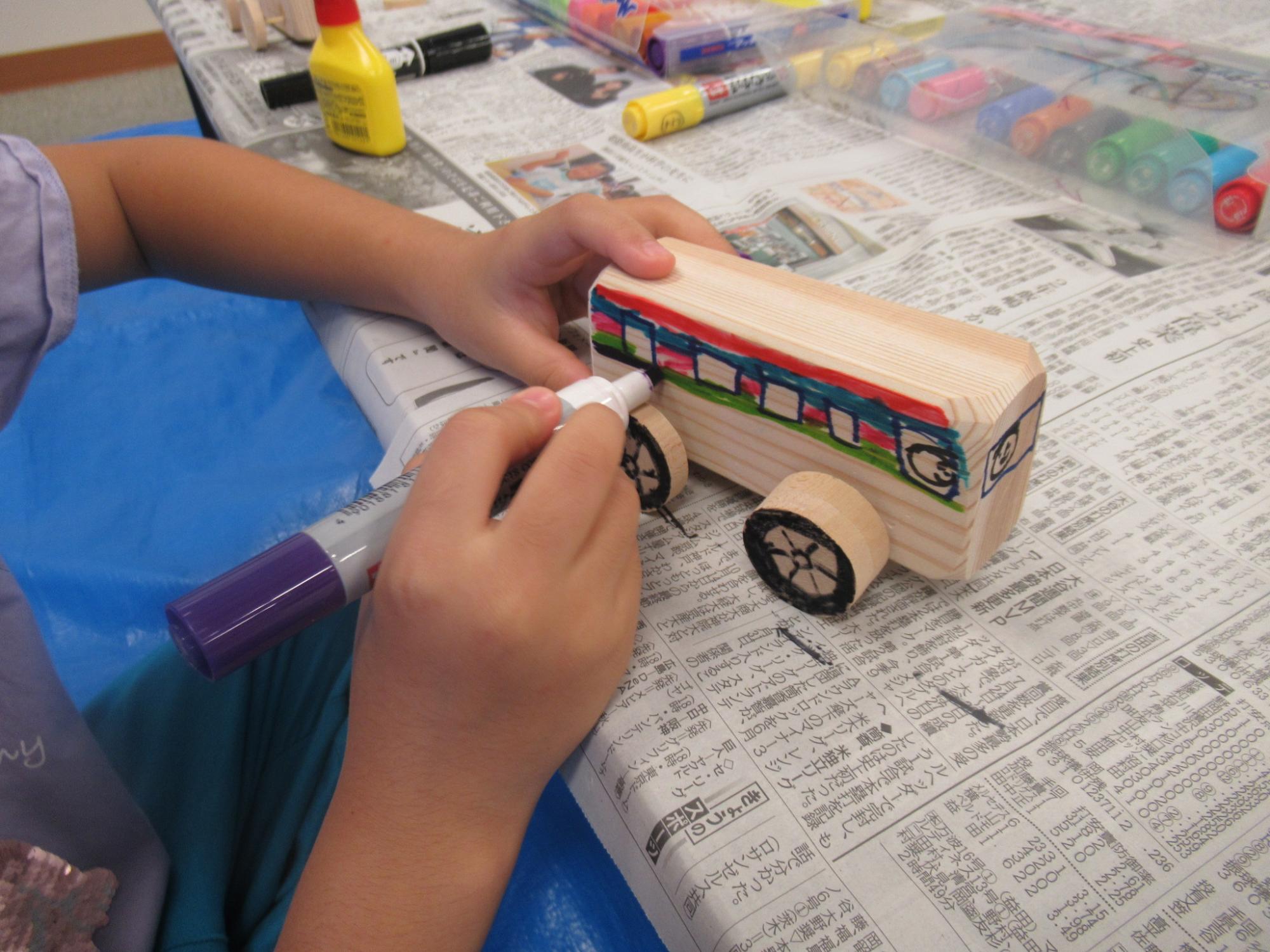 バスの形をした木のおもちゃに子どもがマジックで絵を描いたり色を塗ったりしている写真