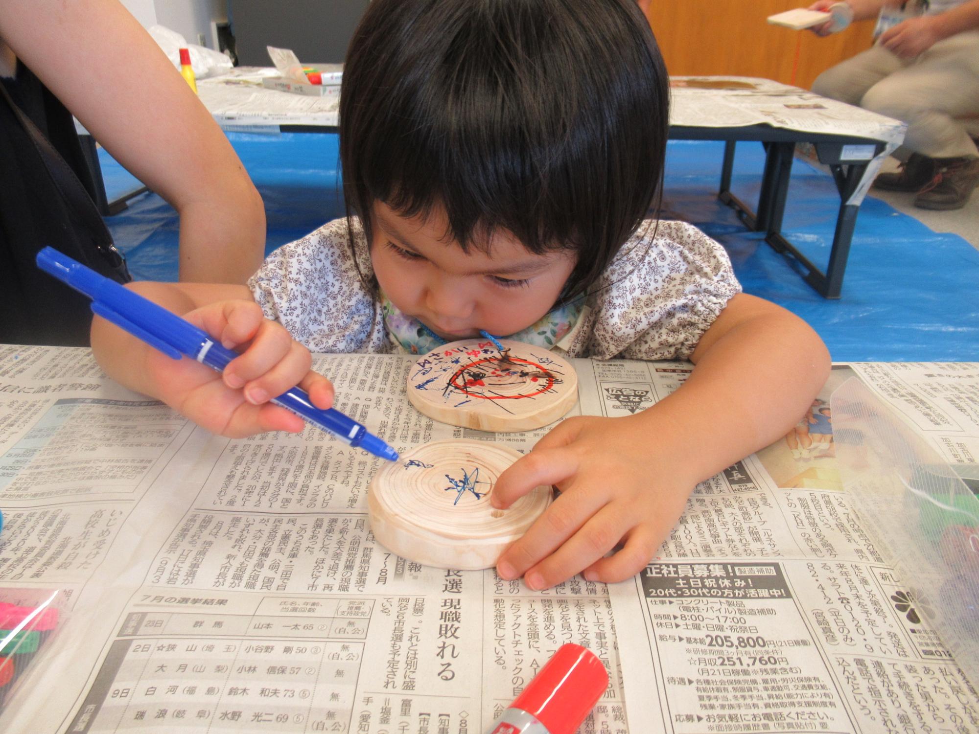 丸い形の木の板に子どもがマジックで絵を描いたり色を塗ったりしている写真