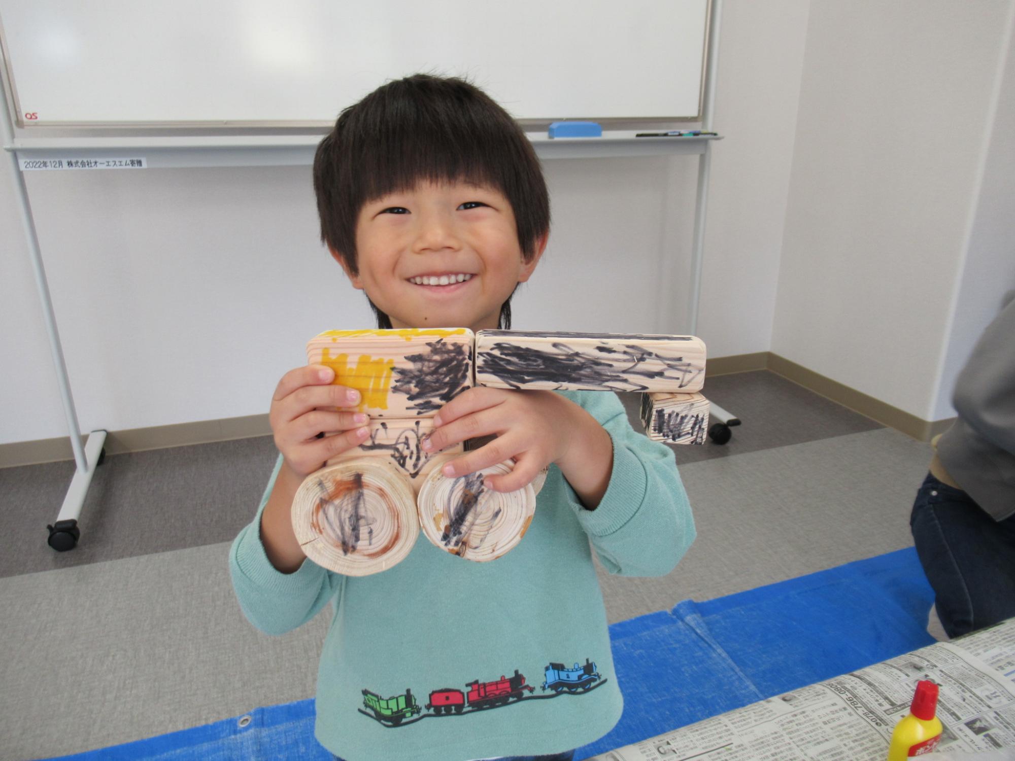 丸や四角の木の板を組み合わせて昆虫の形にした作品を子どもが見せている写真