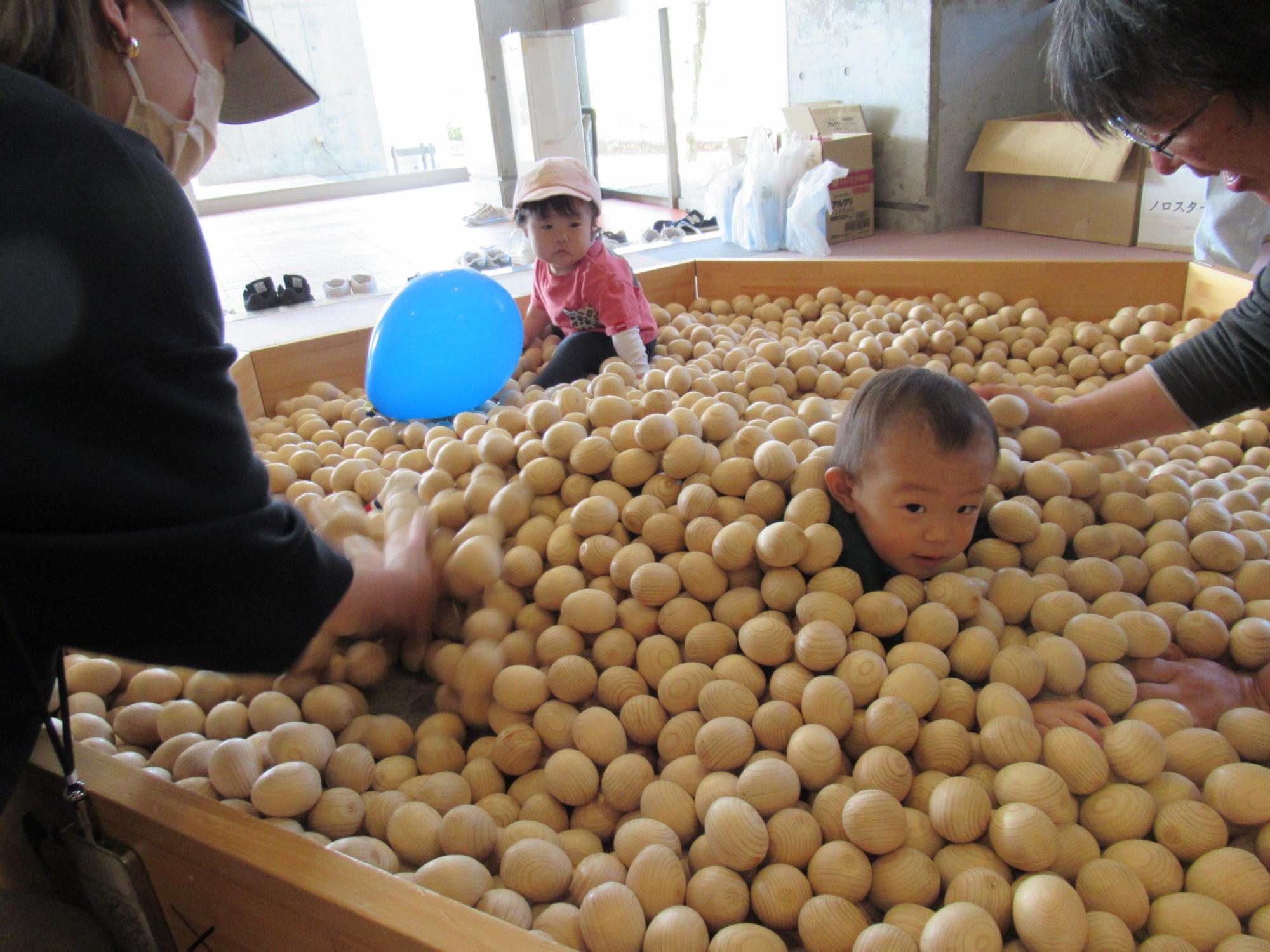 木のボールプールに入って子どもが泳ぐように進んでいる写真