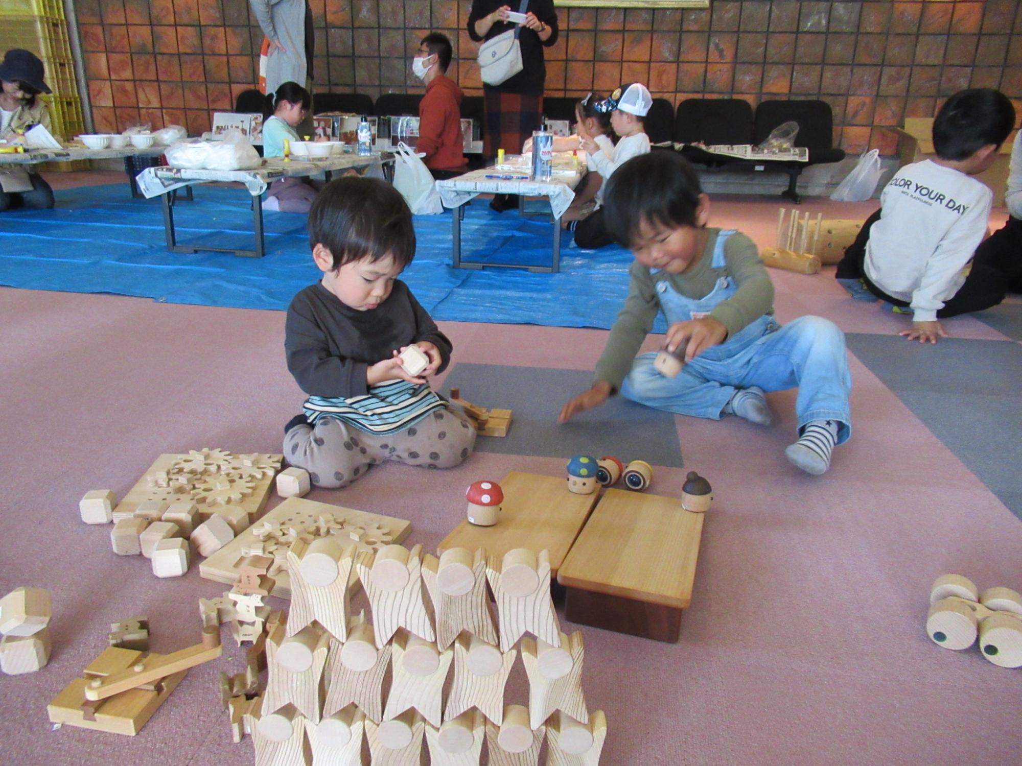 傾けた木の板の上を自動で進む木のおもちゃの仕組みを調べようと子どもがおもちゃの底面を触っている写真