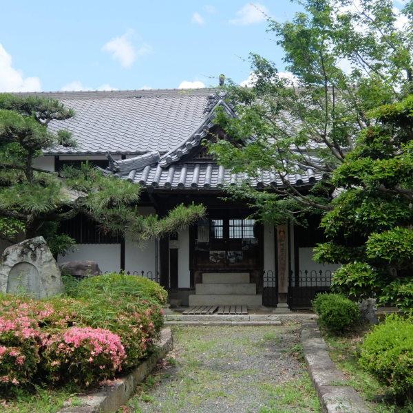 庭に松の木、ツツジが植えられていて、瓦の屋根と白い壁の伝統的な日本家屋の玄関の写真