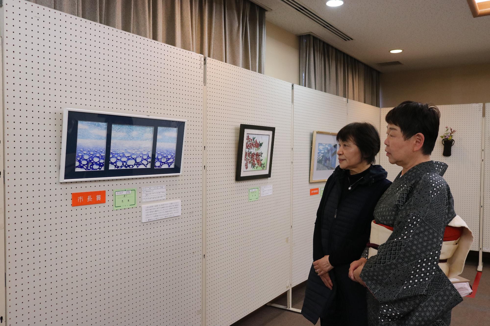 美術展会場に展示されている作品を2人の来場者が一緒に鑑賞している写真
