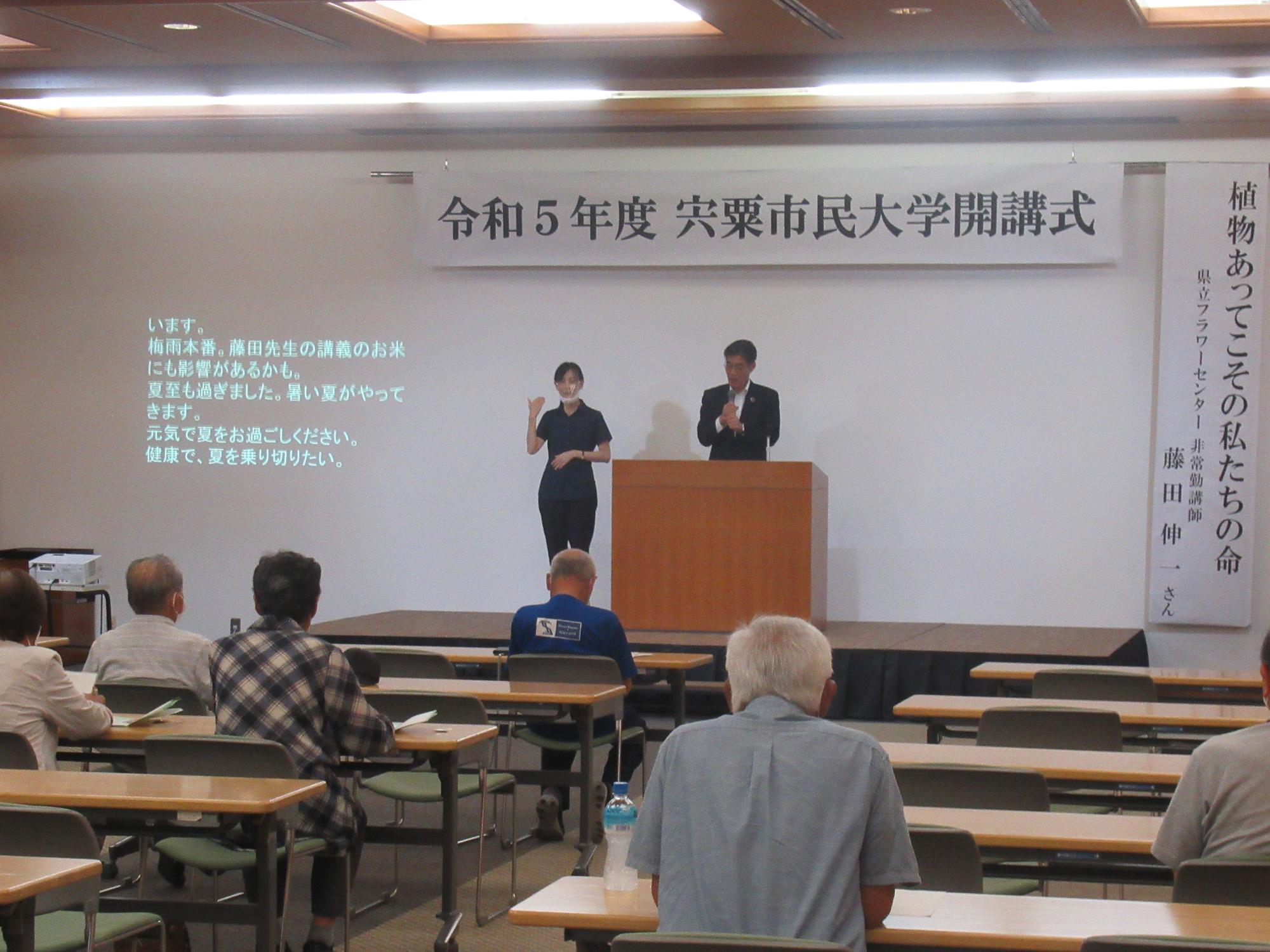 講演会の会場で市民大学の参加者が中田教育長の挨拶を聞いている写真