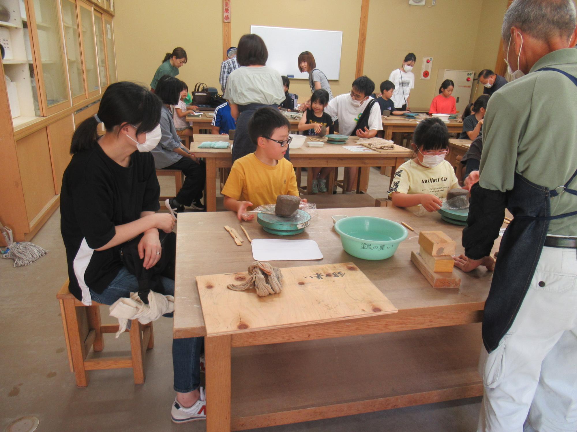 指導員に教わりながら粘土の形を整えていく参加者たち