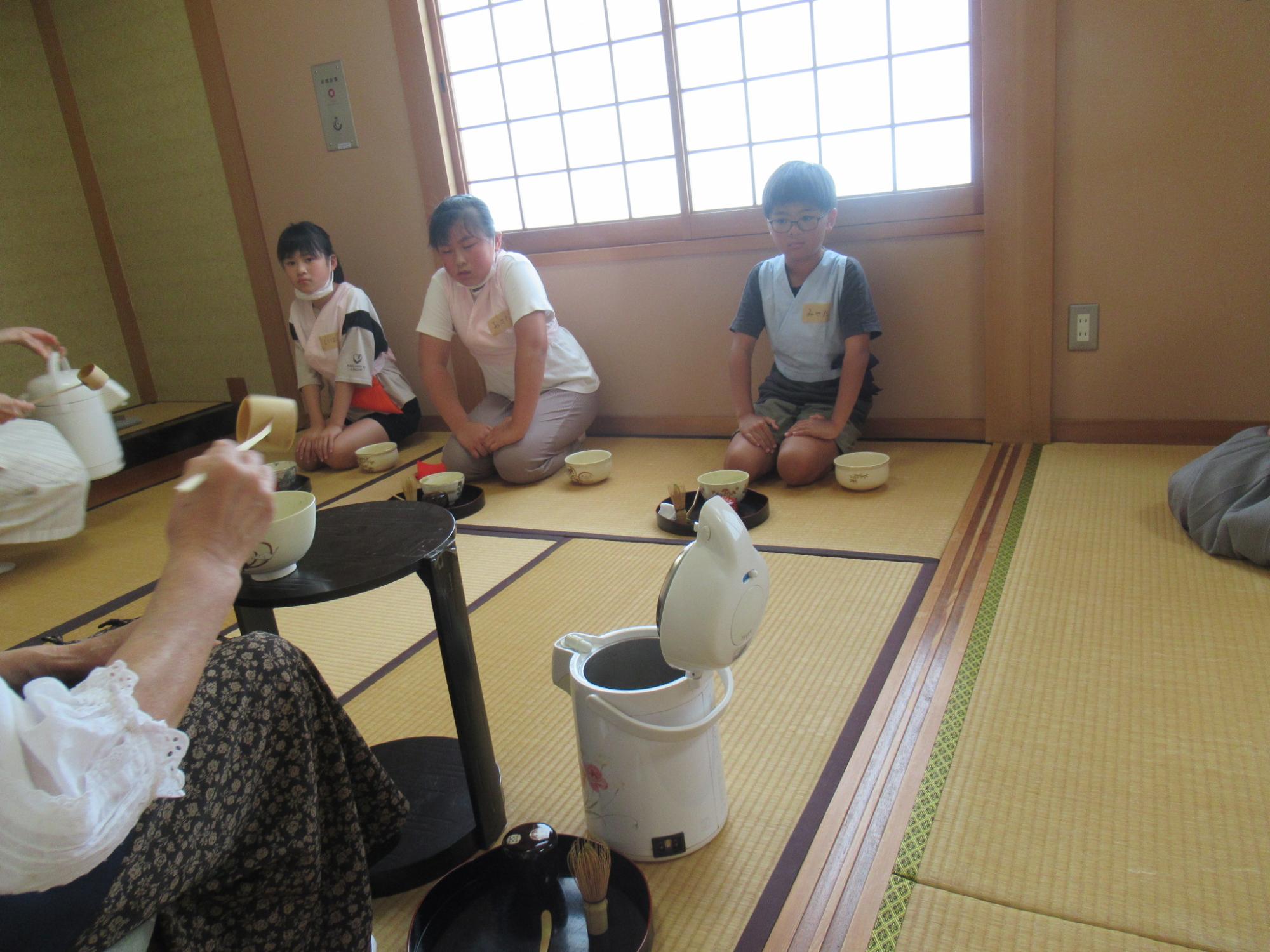 たたみの上に正座して子どもたちがお茶の作法についての話を聞いている写真