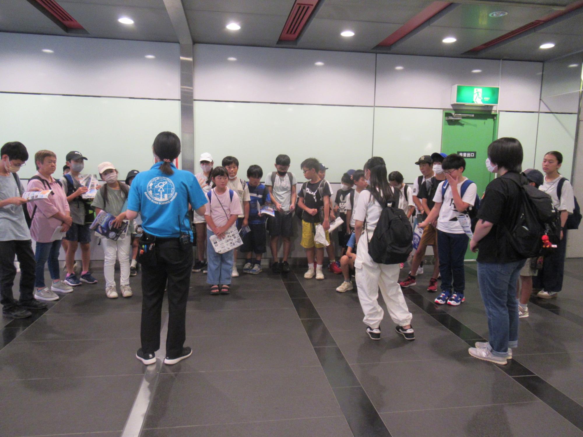 参加者がバンドー神戸青少年科学館の職員から館内の説明を聞いている写真