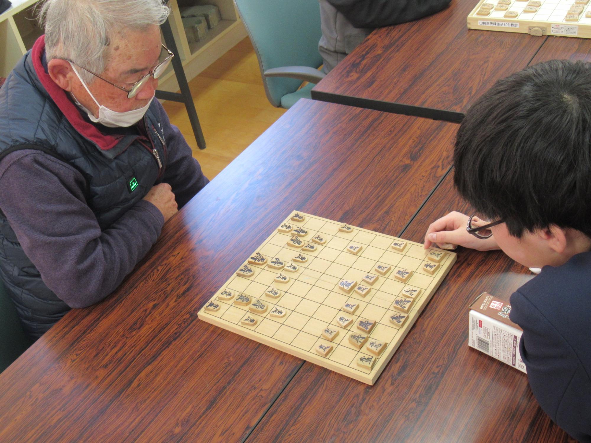 将棋教室に参加者がボランティアの指導員と向かいあって対局している写真