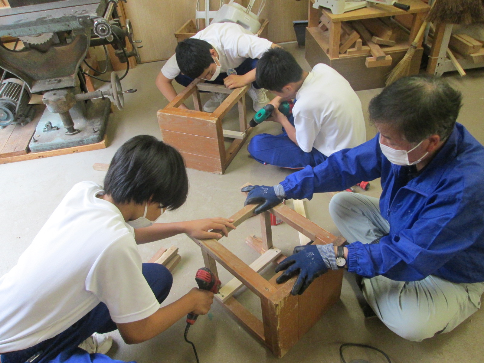 指導員の指示を聞きながら木製の椅子を修理する中学生たちの写真