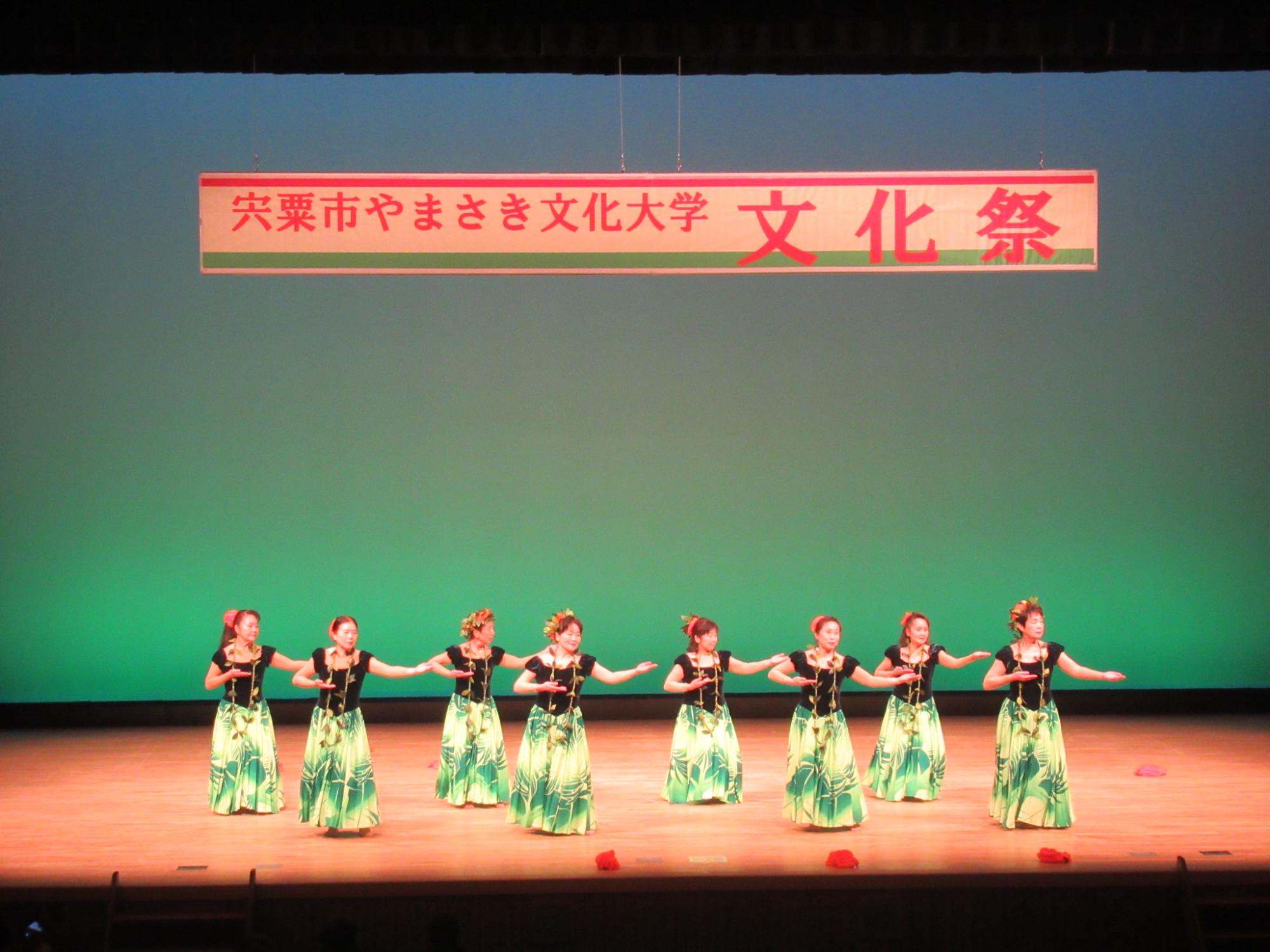 ステージ上でフラダンスを披露するフラダンス部の学生らの写真