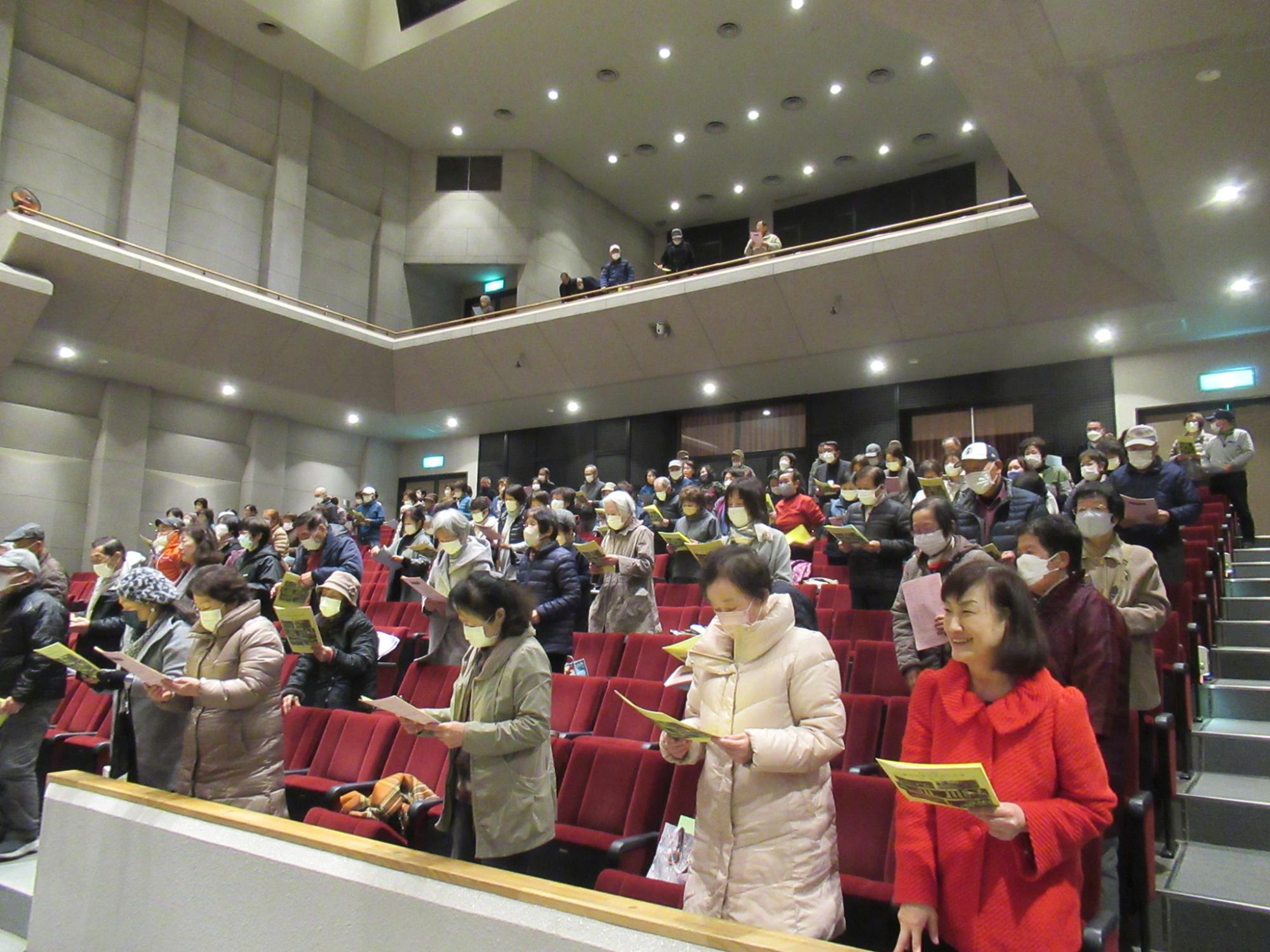 学園生らが山崎文化会館のホール座席上で学園歌を斉唱している写真