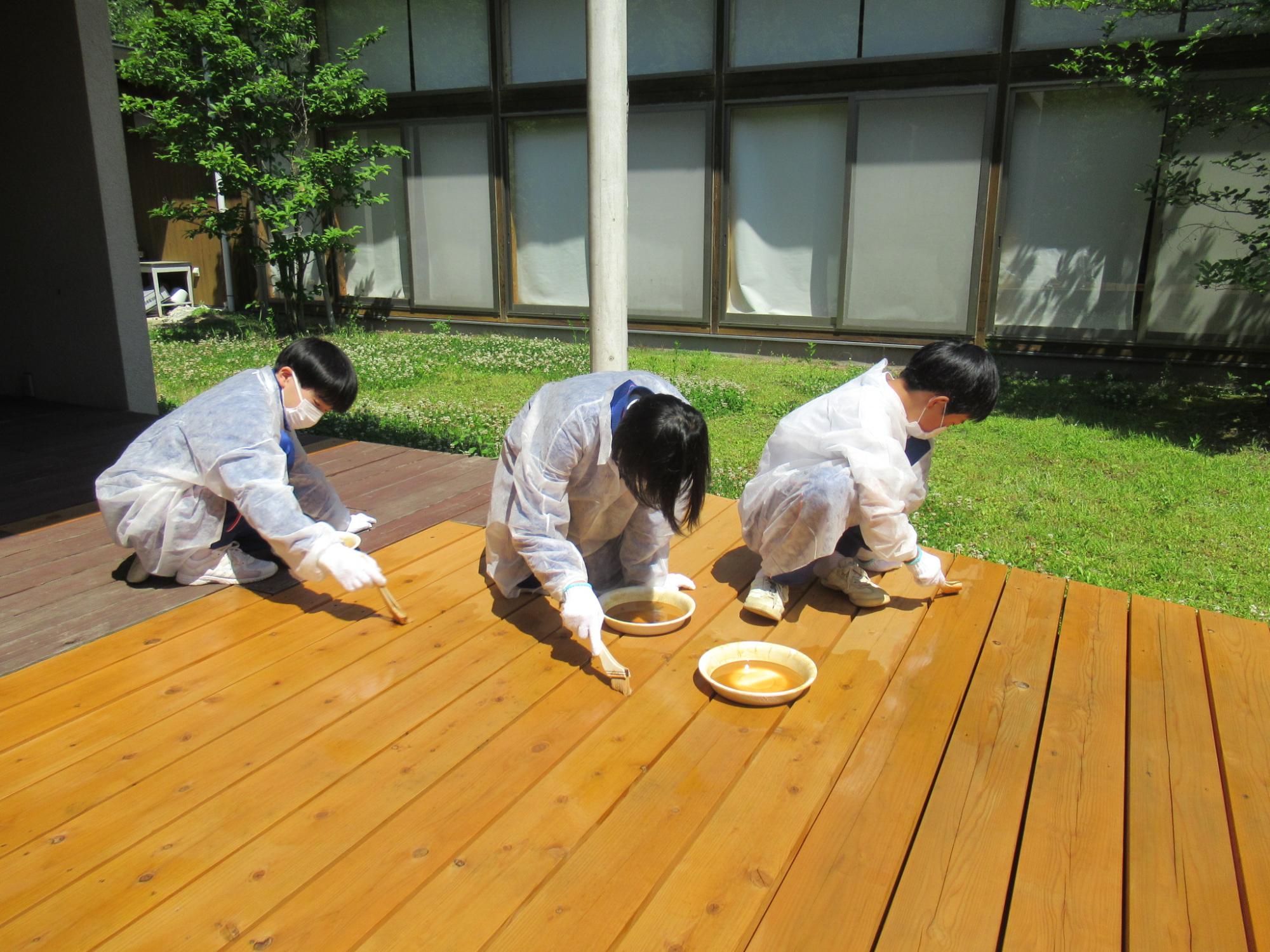生徒らがウッドデッキに防腐剤を塗っている写真