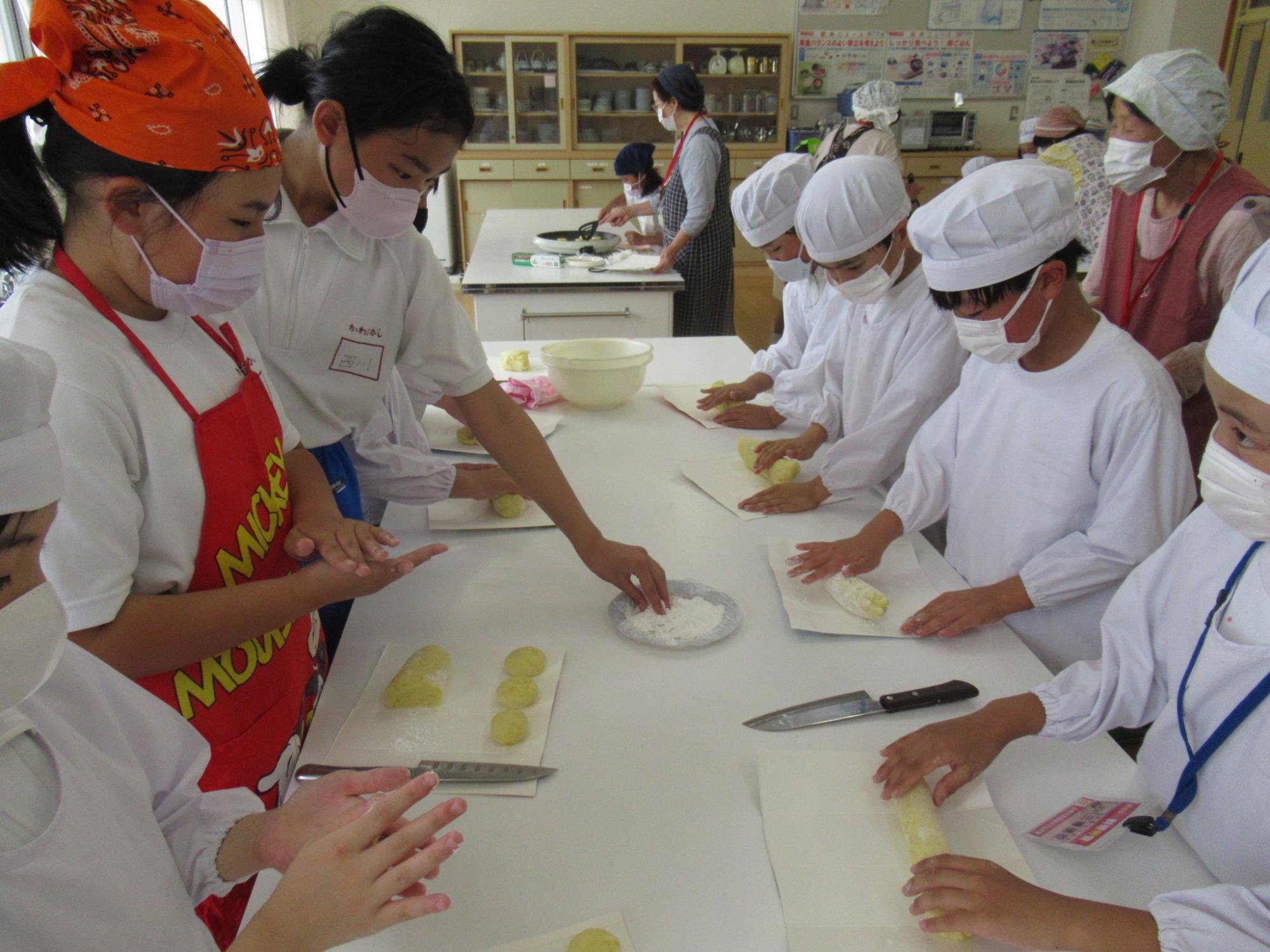 給食エプロンなどを着用した児童らがじゃがいもを潰して成形している写真