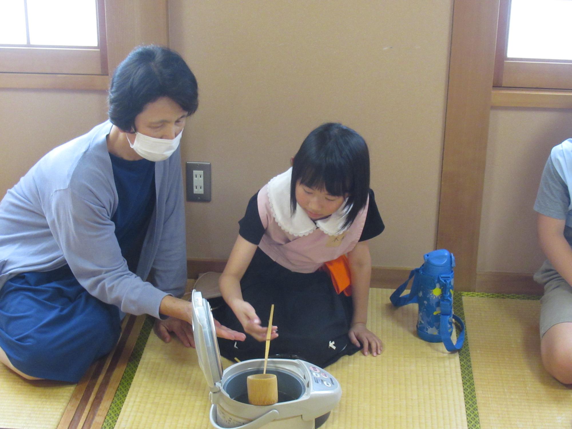 講師の方に教わりながら柄杓でお湯をくみ上げる参加者